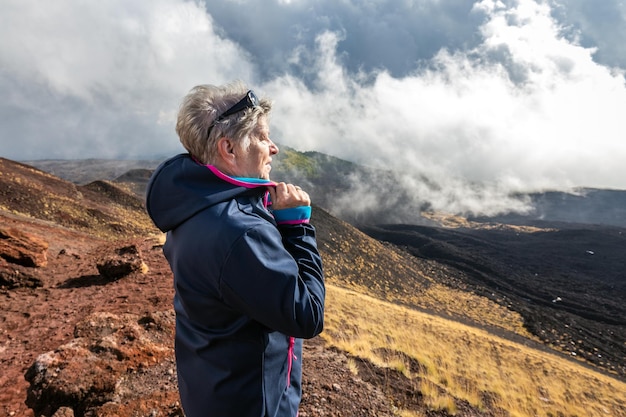 Viajante idosa admirando a paisagem vulcânica de tirar o fôlego do Etna coberto de nuvens em Catania, Sicília, Itália.