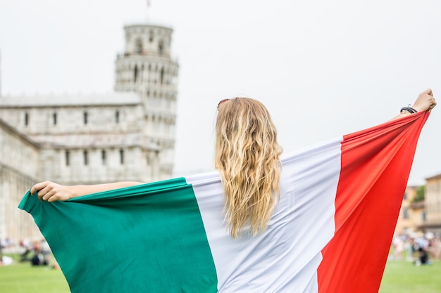 Viajante jovem adolescente com bandeira italiana antes da torre histórica na cidade de Pisa - Itália.