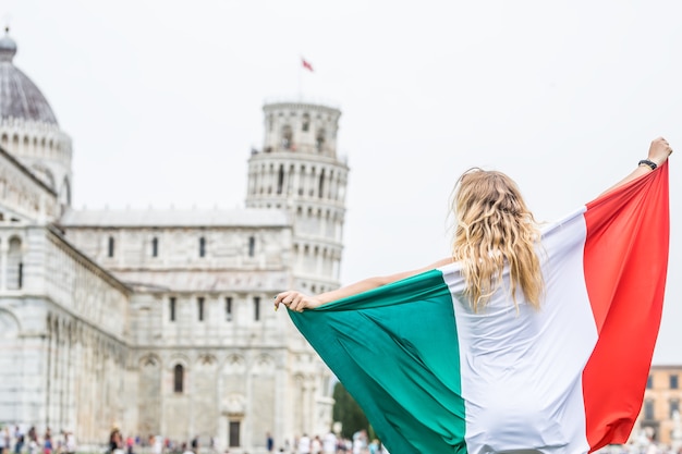 Viajante jovem adolescente com bandeira italiana antes da torre histórica na cidade de Pisa - Itália.