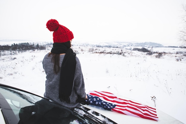 Viajante jovem adulta sentada no capô do carro suv com bandeira dos eua