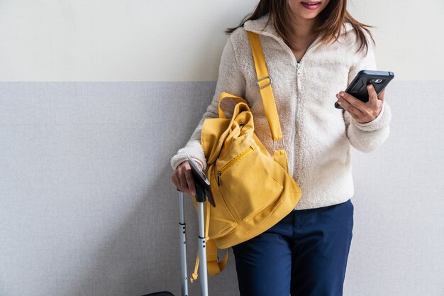 Viajante jovem com bagagem e mochila usando smartphone no aeroporto