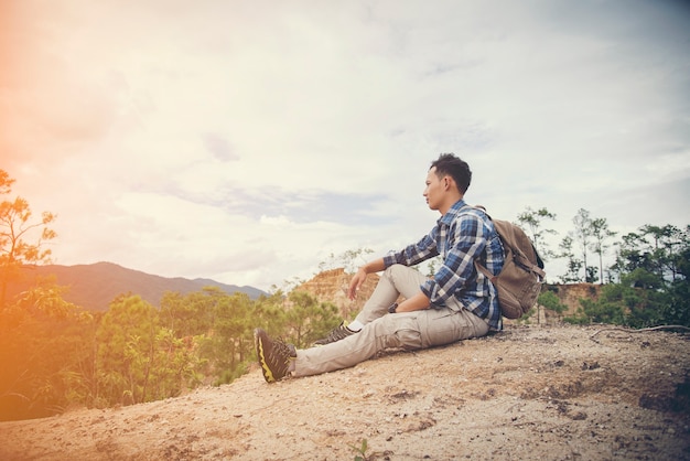 Viajante jovem com mochila relaxante ao ar livre com montanhas rochosas no fundo Férias de verão e conceito de caminhada de estilo de vida.