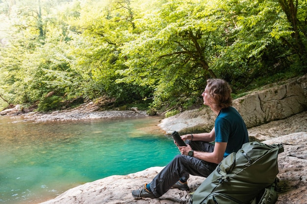 Viajante jovem com mochila relaxante nas rochas do lago de montanha