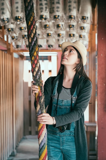 Viajante jovem e bonita toca a campainha para ganhar a atenção do espírito kami no templo shitennoji. turista garota pegando corda para obter bênção no santuário budista osaka japão. senhora elegante enfeitando no xintoísmo