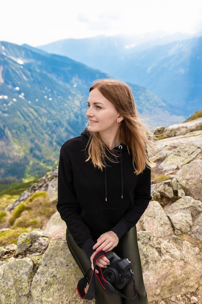 Viajante jovem garota loira com uma mochila azul levantada e apreciando a paisagem de montanha verde