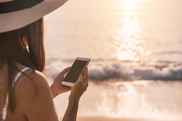 Viajante jovem usando telefone celular na praia tropical no conceito por do sol, férias e verão