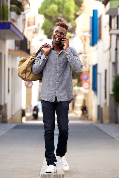 Viajante masculino africano novo do comprimento completo que anda fora e que fala o telefone celular