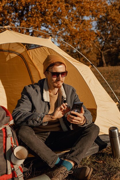 Viajante masculino usando smartphone em barraca de acampamento na floresta no dia ensolarado de outono