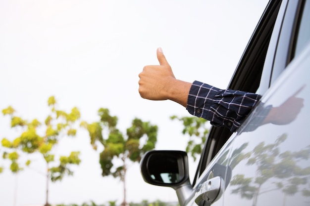 Viajante pronto para sair dirigindo um carro na estrada mostrando o polegar para cima ao ar livre