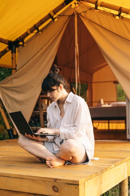 Viajante sentada ao lado da barraca de acampamento e usando notebook trabalhando