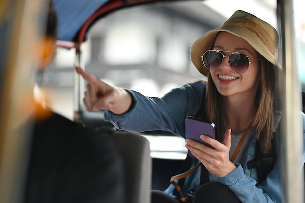 Viajante sorridente usando smartphone para ajudar o turismo sobre o mapa de viagens enquanto está sentado no transporte público de tuk tuk na tailândia