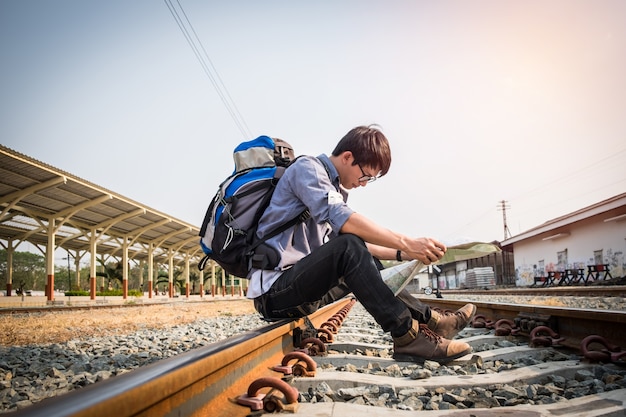 Viajante usando mochila segurando o mapa na estrada de ferro na estação de trem, tom vintage. Conceito de viagem.