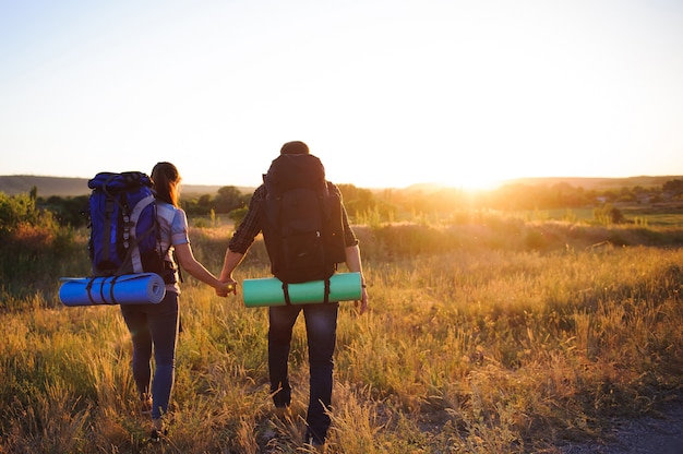 Viajantes com mochila andando no pôr do sol, vista traseira.