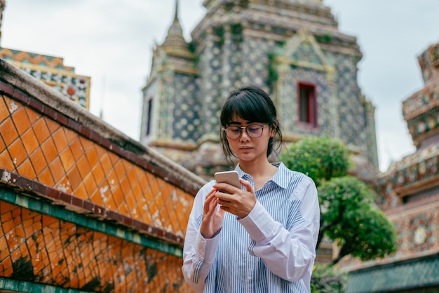 Viajantes de mulher asiática usam smartphone para verificar sua foto perto do antigo pagode edifício fundo