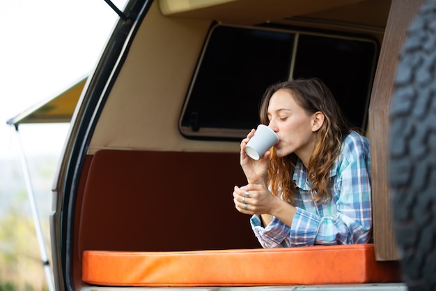 Viajantes de mulher bonita caucasiana feliz desfrutam de café de manhã na natureza, férias em carro de acampamento