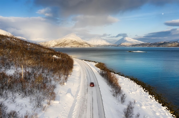 Viajar en coche en Noruega Carretera de montañas y océano al atardecer Coche rojo en la carretera Viajes y aventura