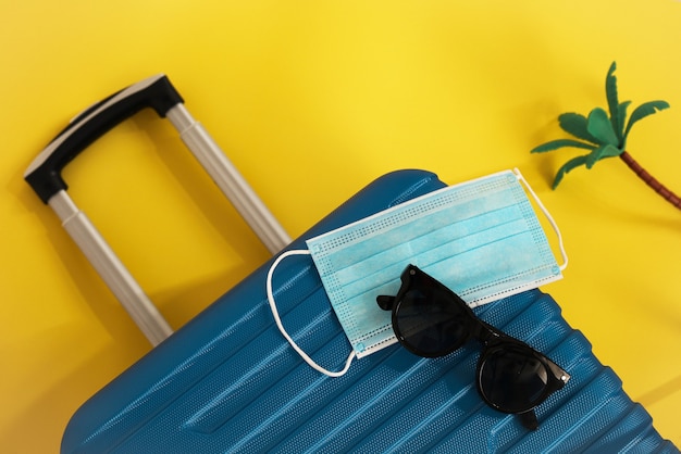 Viajar durante el tiempo de COVID-19. Máscara médica, maleta, gafas de sol, conchas marinas sobre fondo amarillo. Vacaciones, vacaciones en tiempos de corona.