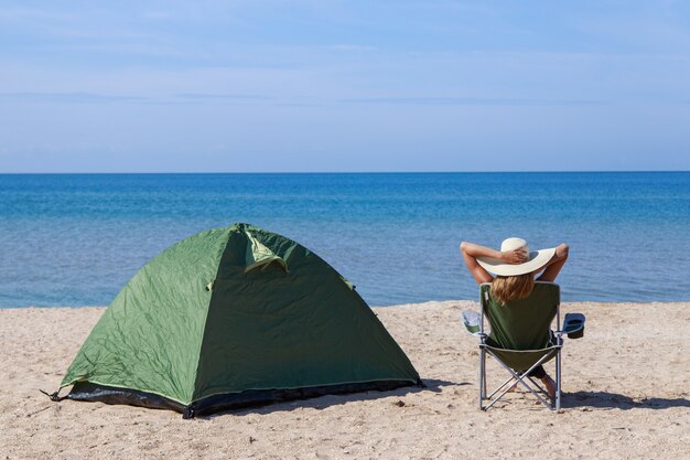 Viaje al mar. acampar en la playa. Vacaciones junto al agua. Hombres y una carpa con una silla turística en la arena.