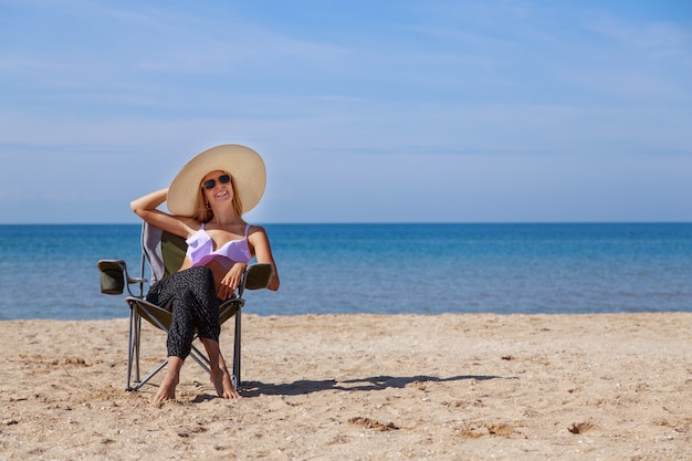 Viaje al mar. chica en traje de baño y sombrero tomando el sol en la playa. turista sentado en la arena. ropa de ocio. copia espacio