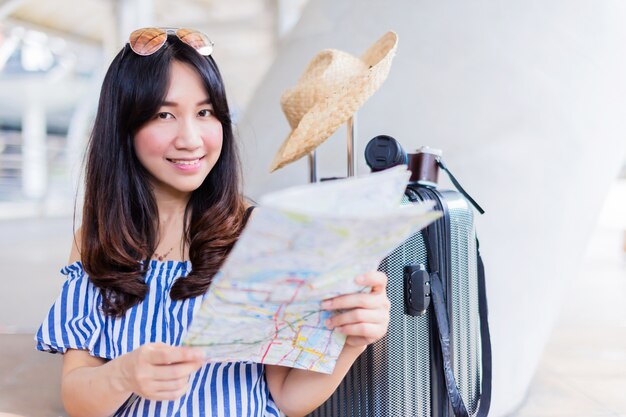 Viaje asiático de la mujer con el mapa en la calle en un día de verano soleado con el fondo de la ciudad de la falta de definición