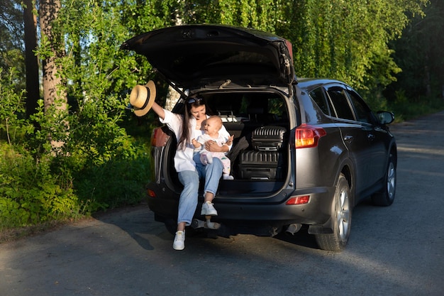 Viaje en automóvil Viajar con un niño en automóvil Madre e hija se sientan en un automóvil con el maletero abierto