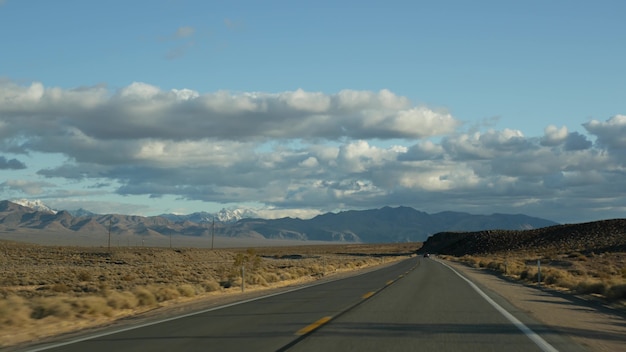 Viaje por carretera, conduciendo en automóvil desde Death Valley hasta Las Vegas, Nevada, EE. UU. Haciendo autostop viajando por América. Viaje por carretera, atmósfera dramática, nubes, montaña y desierto de Mojave. Vista desde el coche