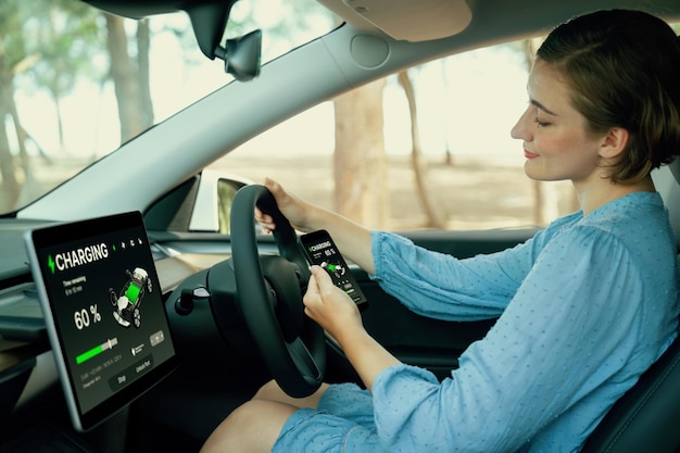 Viaje por carretera de vacaciones con un concepto de automóvil respetuoso con el medio ambiente Mujer consciente del medio ambiente en el asiento del conductor comprobando el estado de la batería del automóvil eléctrico en la pantalla de la tableta o el panel del automóvil durante el viaje en automóvil Perpetuo