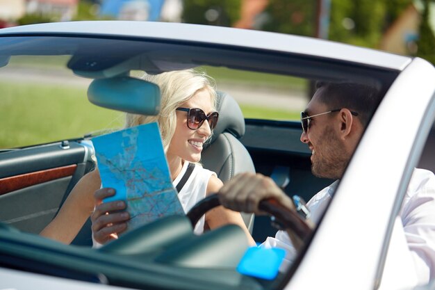 viaje por carretera, viaje, vacaciones de verano y concepto de personas - hombre y mujer felices conduciendo en camión cabriolet con mapa