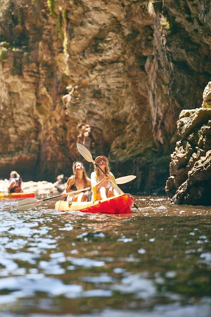 Viaje de caiaque e amigas em uma aventura enquanto estiver em um lago ou mar com vista para a montanha na natureza Mulheres se divertindo enquanto viajam e desfrutam de atividades aquáticas durante uma viagem de férias