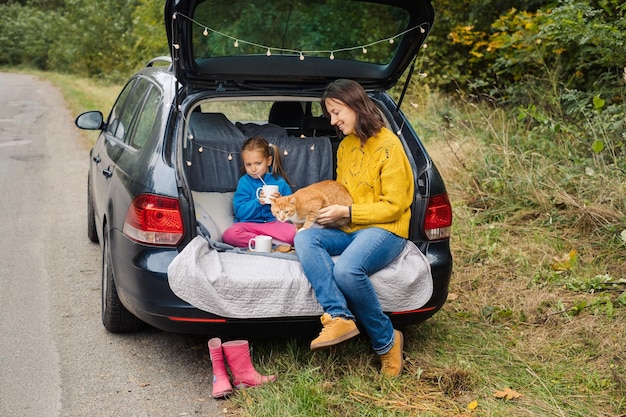 Viaje familiar por carretera con mascota sentada en el baúl del auto y comiendo comida sabrosa