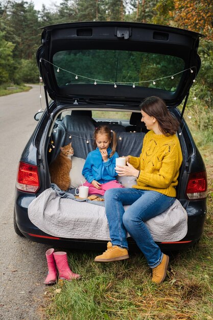 Viaje familiar por carretera con mascota sentada en el baúl del auto y comiendo comida sabrosa