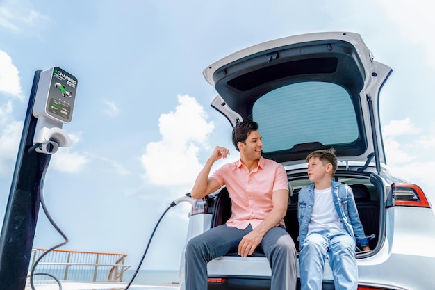 Viaje familiar por carretera vacaciones viajando por el mar con coche eléctrico padre e hijo recargan coche eléctrico con energía verde y limpia Viajes naturales y coche ecológico para un medio ambiente sostenible Perpetuo