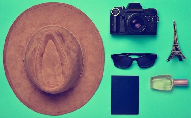 Viaje a Francia, París. Sombrero de fieltro, cámara de cine, gafas de sol, pasaporte, frasco de perfume, estatuilla de recuerdo del diseño de la Torre Eiffel sobre un fondo de papel azul.