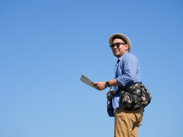 Viaje de hombre asiático con mapa y cámara vintage sobre fondo de cielo azul