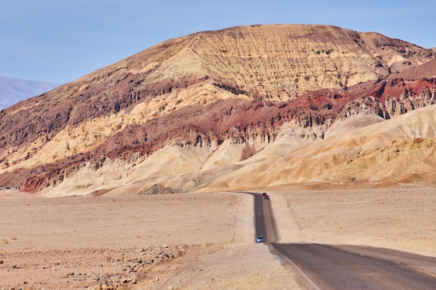 El viaje por un largo camino recto en un desierto que conduce a grandes montañas coloridas