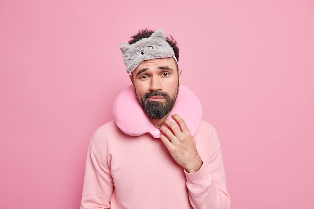 El viaje masculino disgustado soñoliento se ve con expresión cansada usa una almohada de viaje inflada con los ojos vendados alrededor del cuello para dormir en el transporte