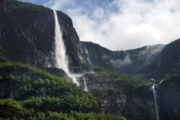 Viaje a Noruega, una cascada fluye desde la cima de una montaña alta contra un cielo nublado.