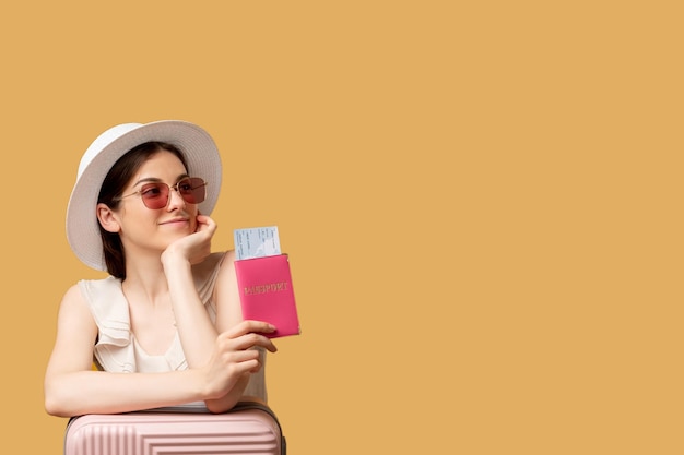 Viaje de verano Viaje de vacaciones Agencia de viajes Antecedentes publicitarios Mujer feliz gafas de sol sombrero maleta inclinada con boletos de pasaporte extranjero mirando espacio de copia aislado en beige