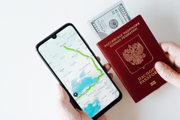 Viaje viaje emigración concepto de vacaciones y turismo Primer plano de la mano que sostiene el teléfono móvil con un mapa en línea y ruta de viaje pasaporte internacional de la federación rusa y vista superior del dinero