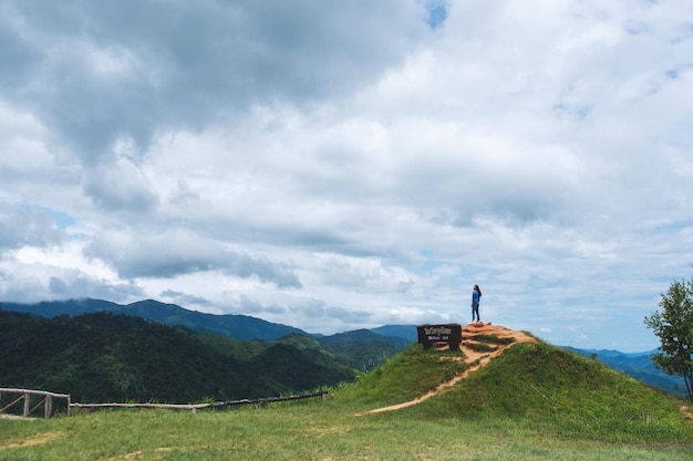 Una viajera parada en la cima de la montaña y mirando una hermosa vista de las montañas verdes