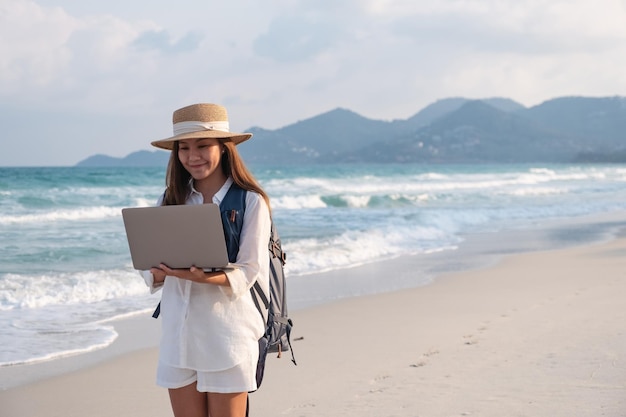 Una viajera que usa y trabaja en una computadora portátil mientras camina por la playa