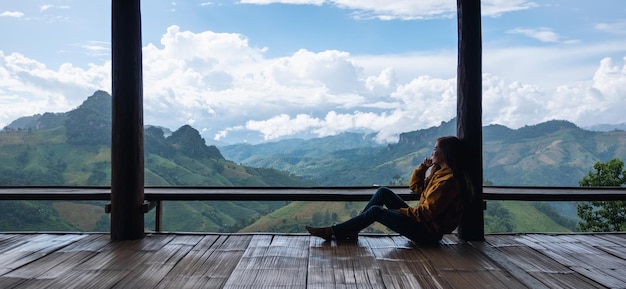 Una viajera sentada y mirando una hermosa vista de las montañas y la naturaleza en un balcón de madera