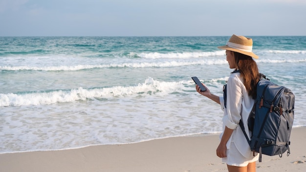 Una viajera sosteniendo y usando un teléfono móvil junto al mar