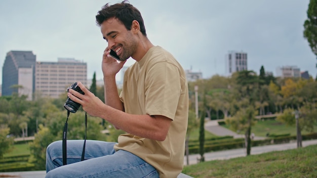 Viajero alegre hablando por teléfono móvil mirando fotos en la cámara en el parque de primer plano