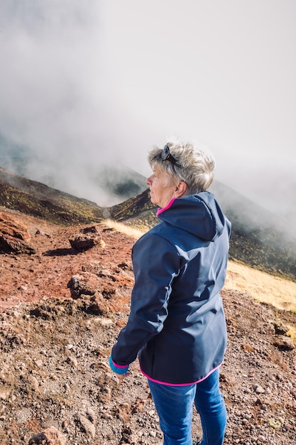 Viajero anciana admirando el impresionante paisaje volcánico del Etna cubierto de nubes en Catania Sicilia, Italia.