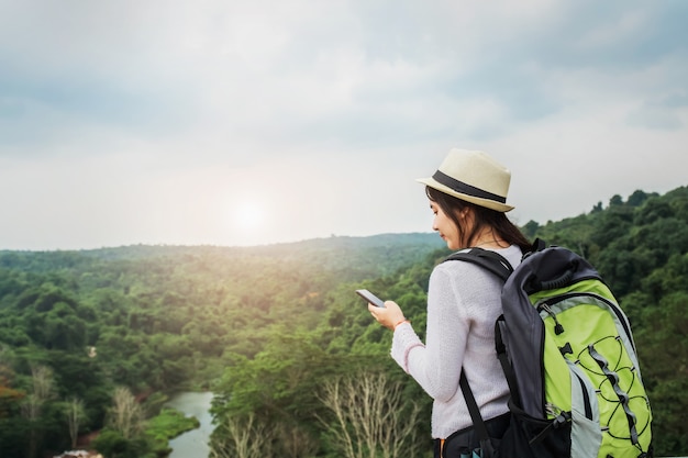 Viajero asiático hermoso de la mujer con la mochila que se relaja en vacaciones en la montaña con usar el móvil