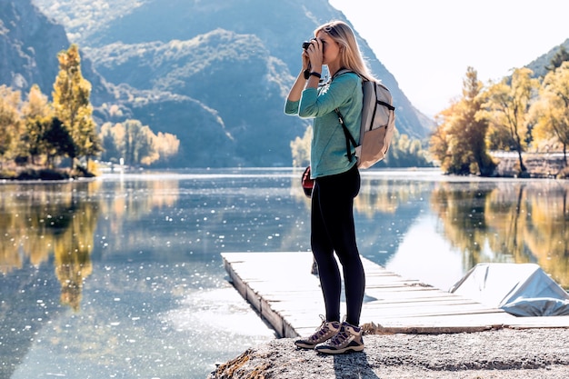 Viajero bastante joven con mochila tomando fotografías con cámara en el lago.