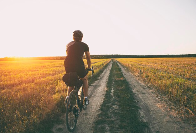 Viajero en bicicleta cabalgando por el campo al atardecer en bicicleta con bolsas