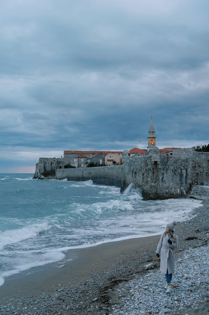 El viajero camina a lo largo de la costa cerca de las murallas de la fortaleza de la antigua ciudad de Budva mirando el