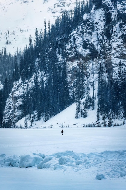Un viajero caminando sobre un lago congelado y una montaña nevada en invierno